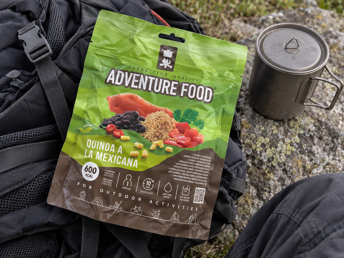 Adventure Food Quinoa a la Mexicana in de verpakking tijdens een pauze onderweg, naast wandeluitrusting.