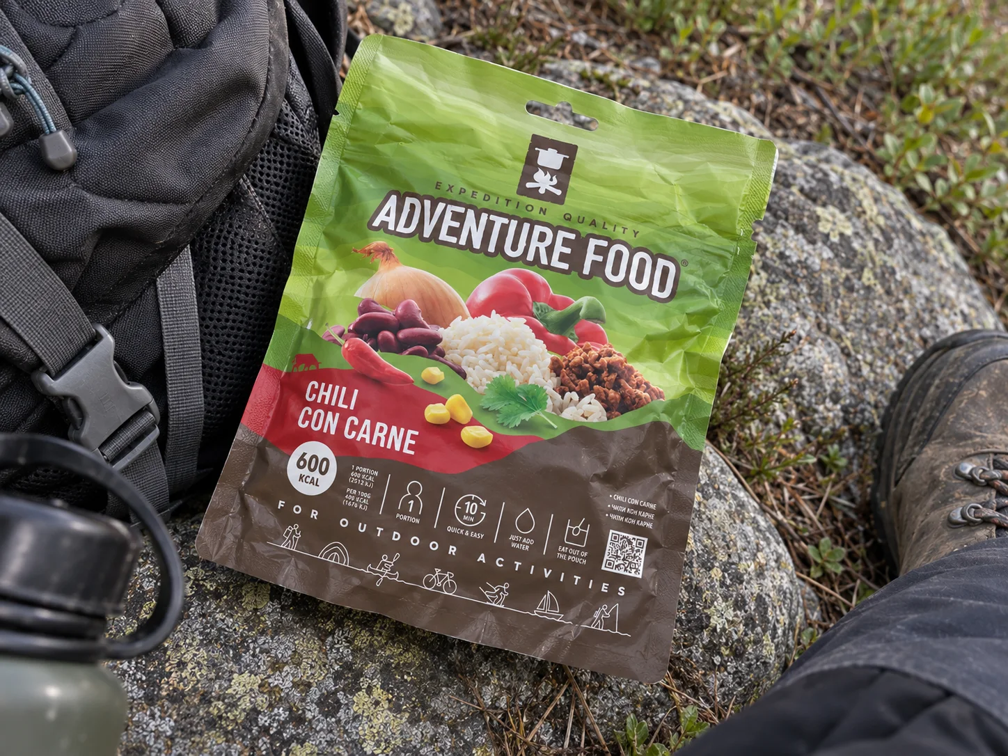 Adventure Food Chili con Carne (New Taste) in de verpakking tijdens een pauze onderweg, naast wandeluitrusting.