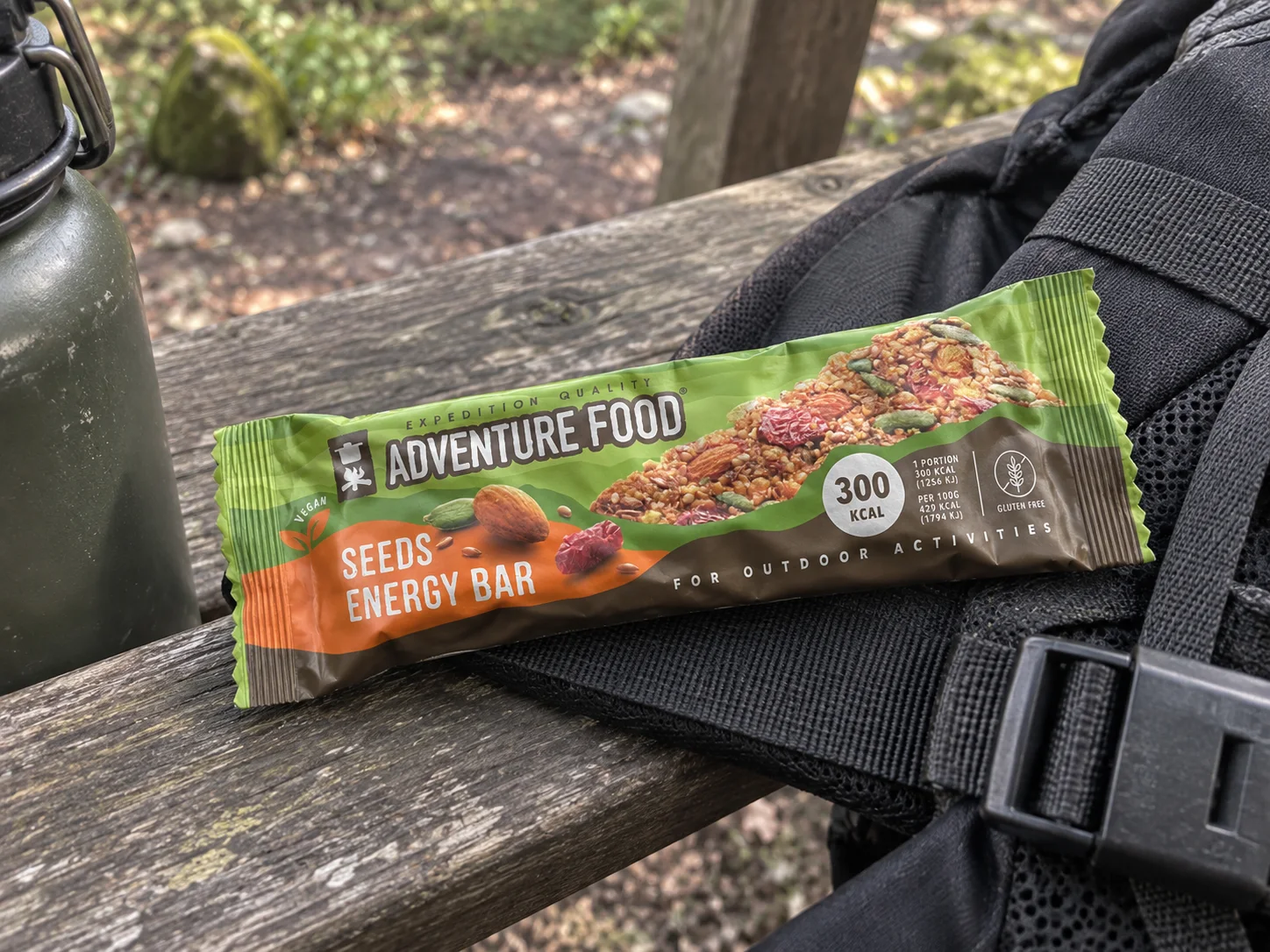 Adventure Food Seeds Energy Bar in de verpakking tijdens een pauze onderweg, naast wandeluitrusting.