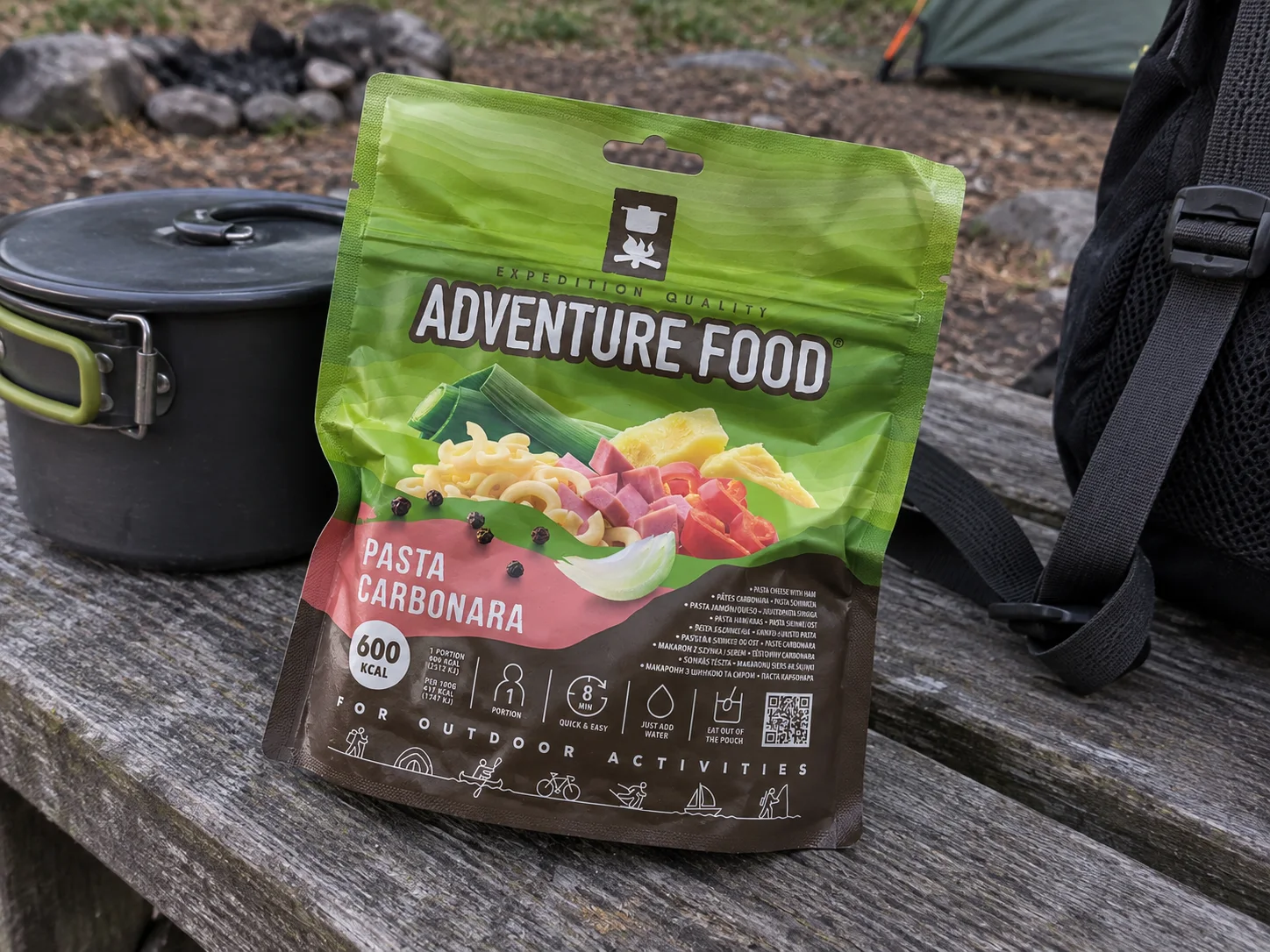 Adventure Food Pasta Carbonara in de verpakking tijdens een pauze onderweg, naast wandeluitrusting.