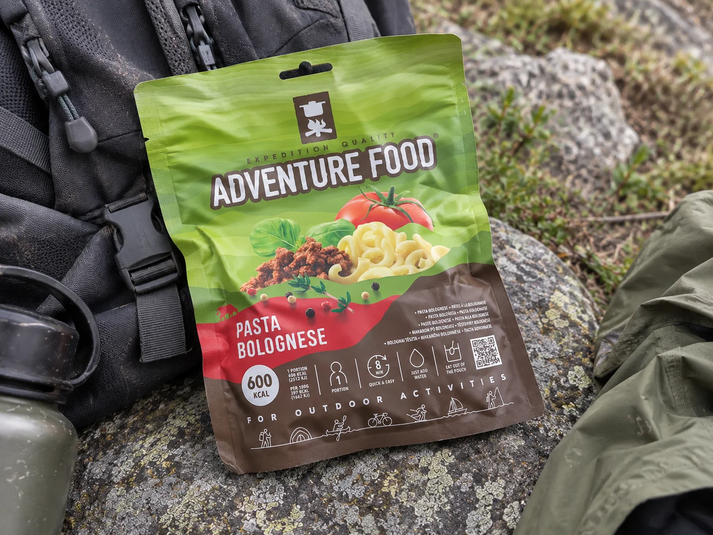 Adventure Food Pasta Bolognese in de verpakking tijdens een pauze onderweg, naast wandeluitrusting.