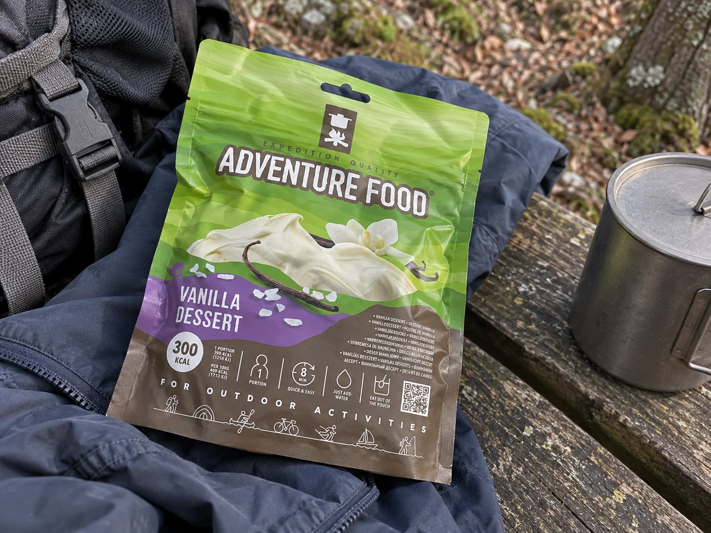 Adventure Food Vanilla Dessert in de verpakking tijdens een pauze onderweg, naast wandeluitrusting.