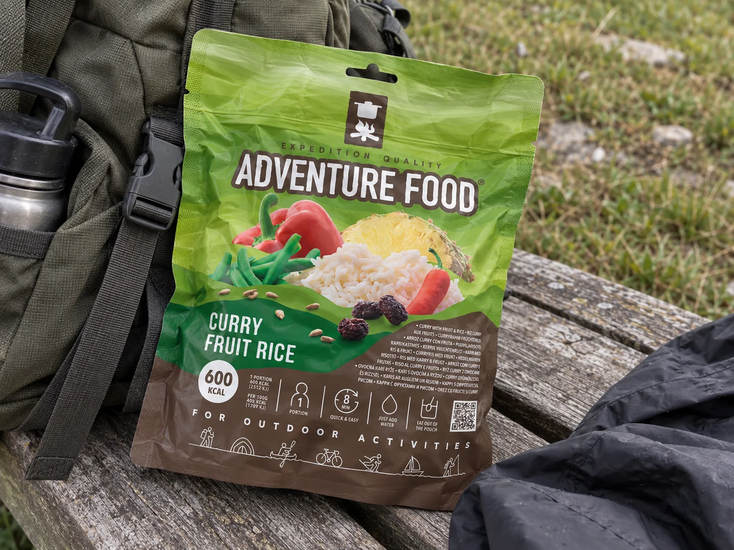 Adventure Food Curry Fruit Rice in de verpakking tijdens een pauze onderweg, naast wandeluitrusting.