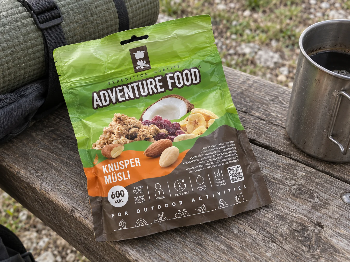 Adventure Food Knusper Musli in de verpakking tijdens een pauze onderweg, naast wandeluitrusting.